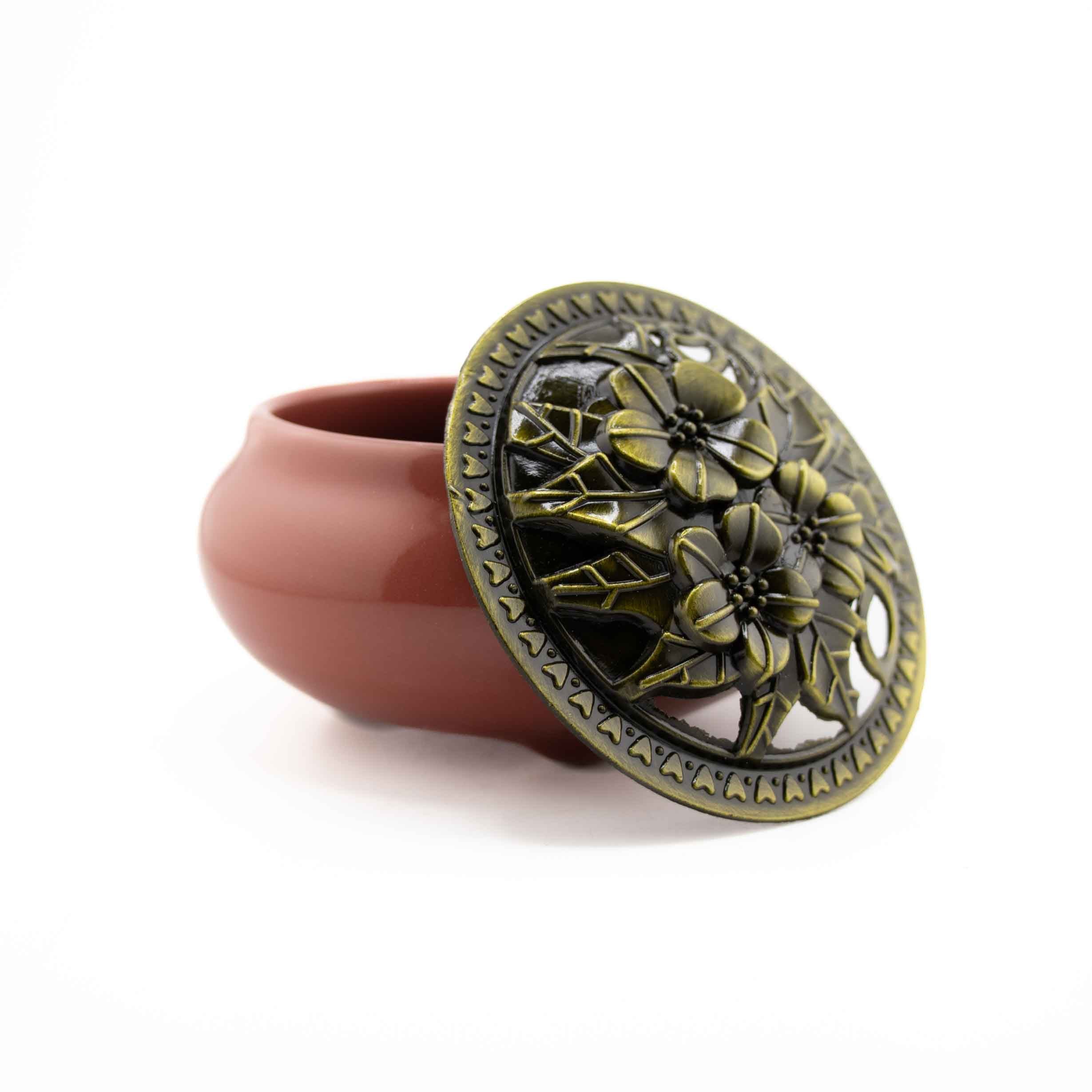 A burgundy-pink ceramic incense burner bowl with an ornamental, bronze-finished floral cutout lid.
