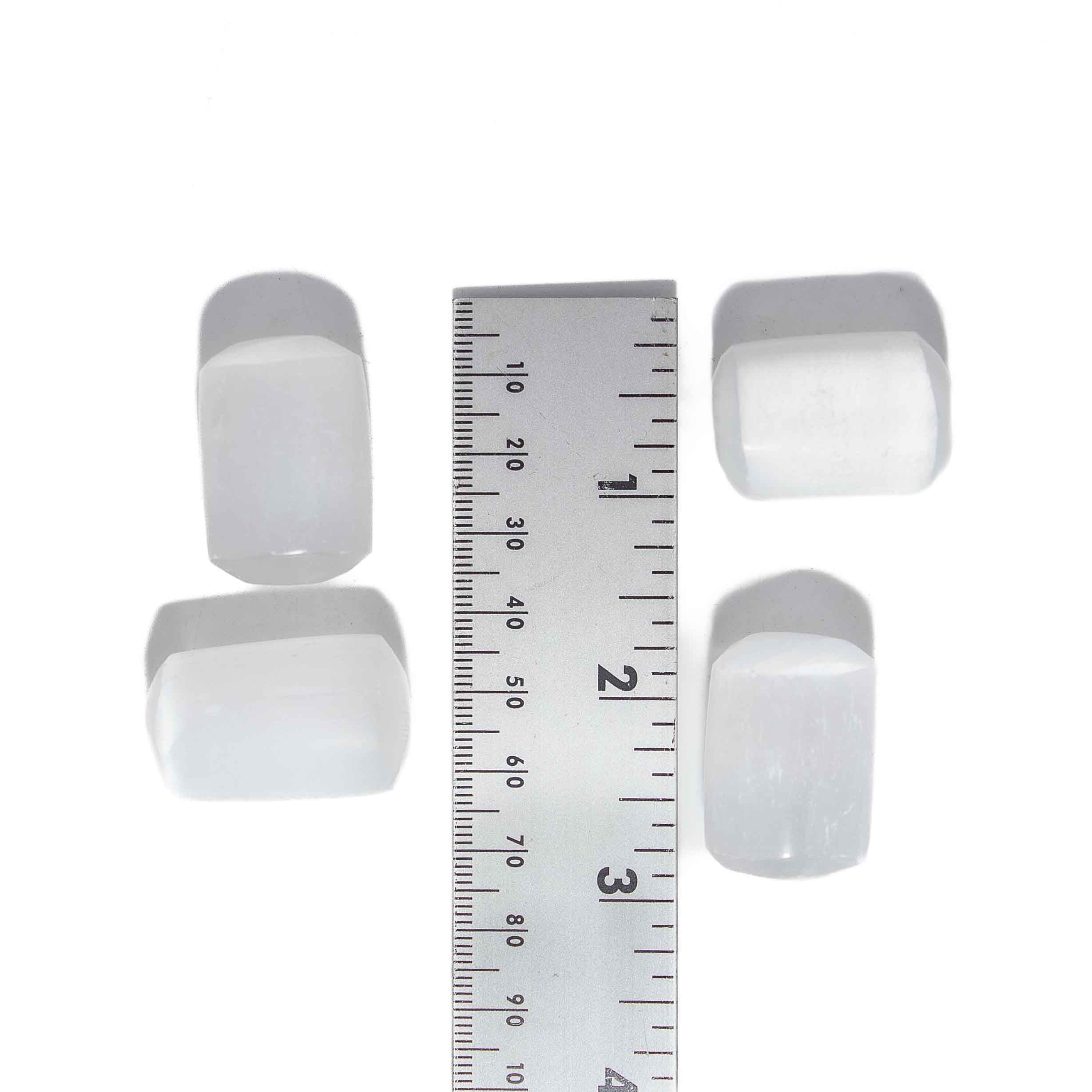 Four 1-inch selenite tumbled stones in white with smooth polished finish, shown alongside ruler for scale on white background.