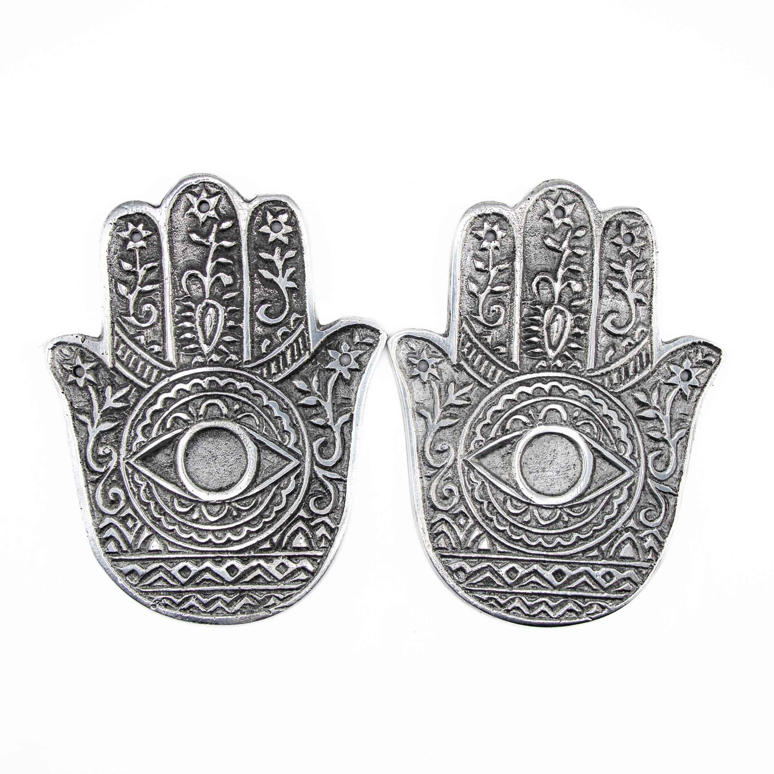 Two silver-toned metal incense burners in the shape of a Hamsa hand, featuring an embossed eye in the center and intricate floral patterns.
