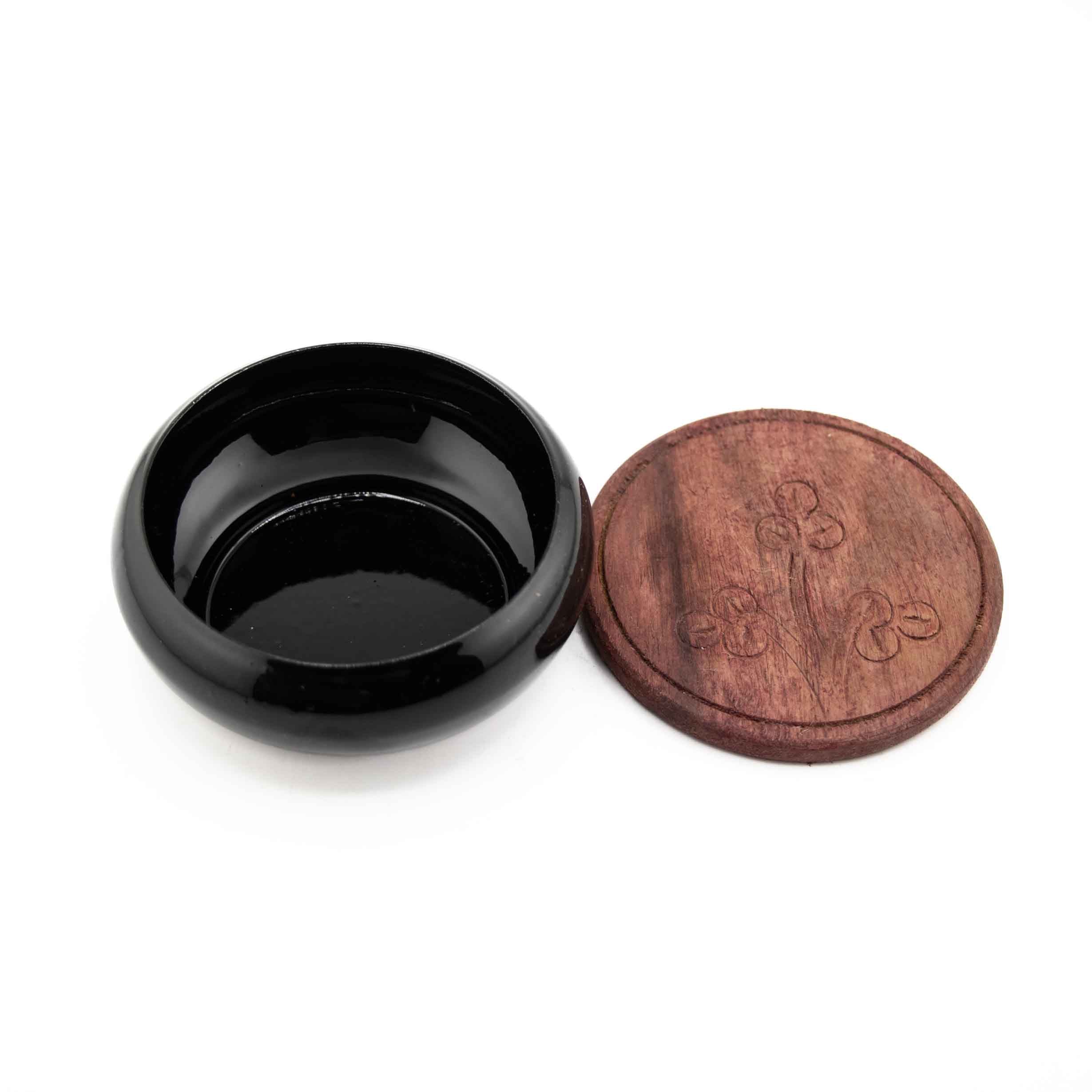 A glossy black metal charcoal burner bowl paired with a circular wooden coaster featuring an engraved floral design.