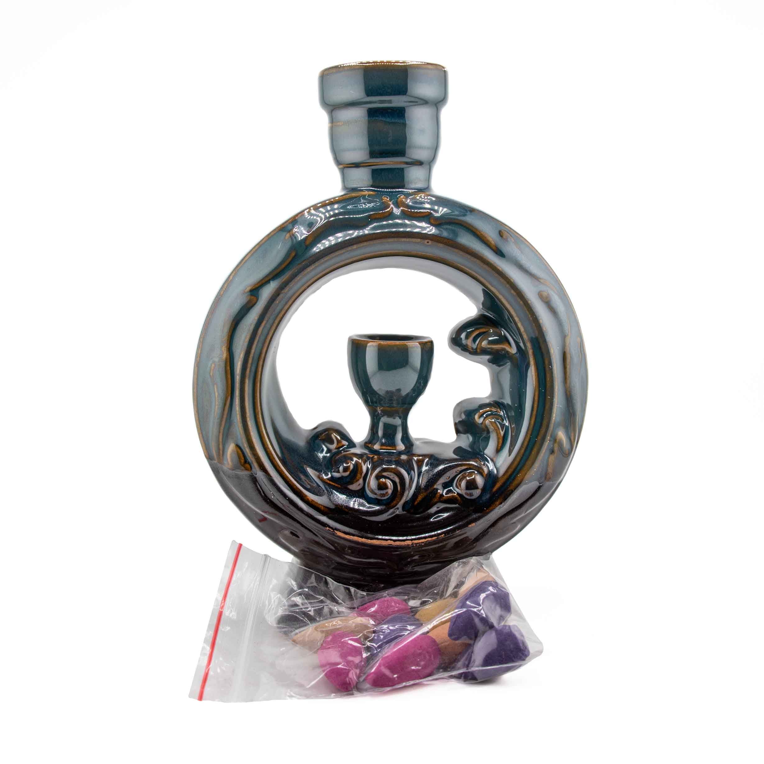 A circular ceramic backflow incense burner with a waterfall design in a dark glazed finish, featuring an integrated chalice-style holder and a bag of incense cones.